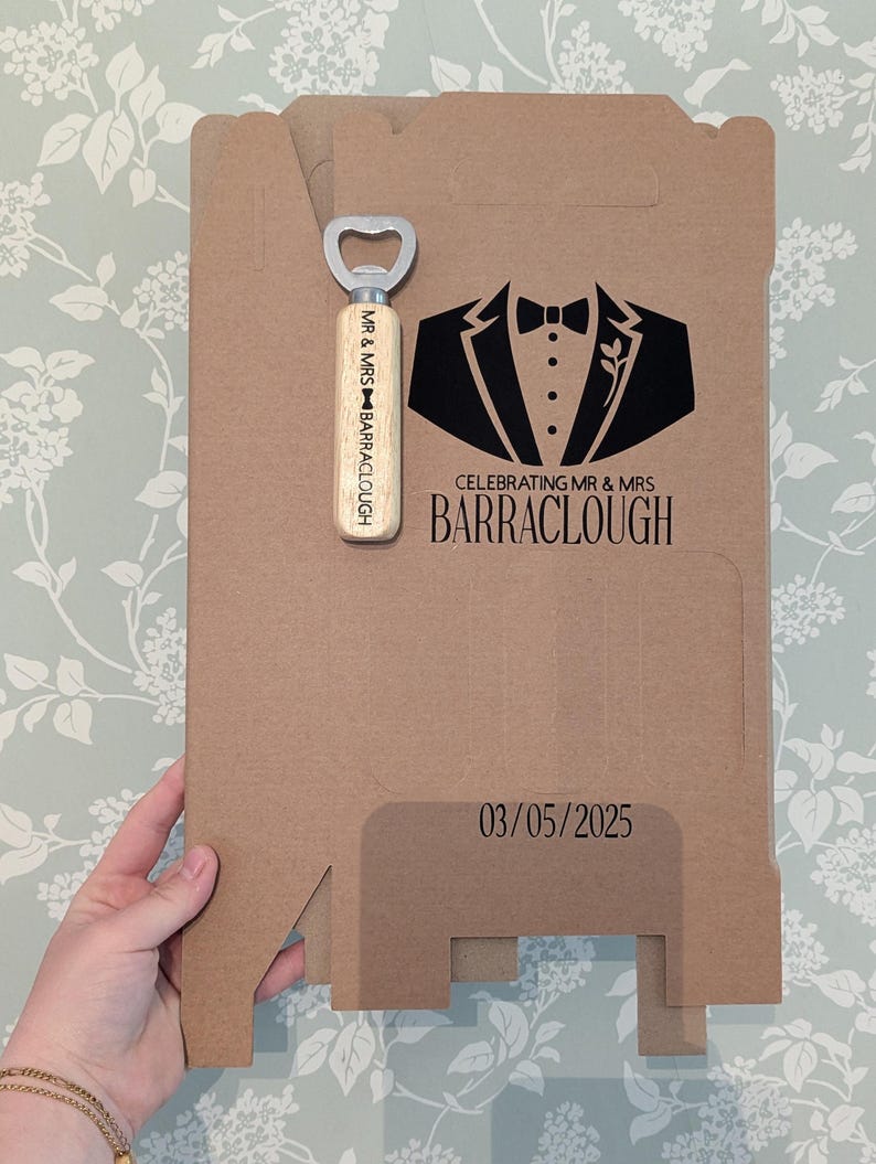May include: A brown cardboard box with a black tuxedo graphic and the text "Celebrating Mr. & Mrs. BARRACLOUGH 03/05/2025". A wooden bottle opener with the text "Mr. & Mrs. BARRACLOUGH" is included.