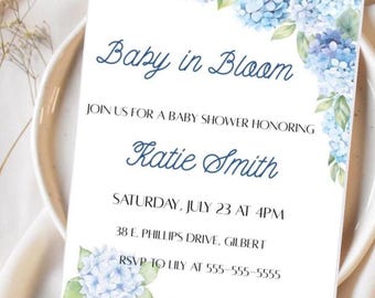 May include: A baby shower invitation with a watercolor design of blue hydrangeas. The invitation reads "Baby in Bloom" and includes the name "Katie Smith", the date and time of the shower, the address, and the RSVP information. The registry is listed as Zola.com.