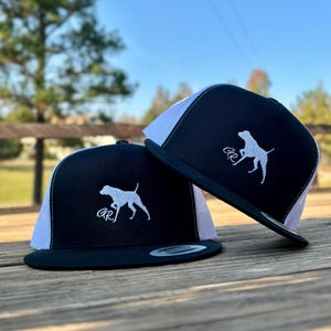May include: Two black and white baseball caps with a white mesh back. The caps have a white embroidered dog silhouette and the letters "GR" on the front.