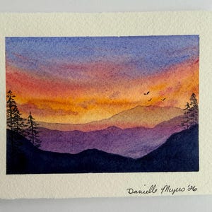 May include: Watercolor painting of a sunset over a mountain range. The sky transitions from blue to orange and red, with silhouetted trees on either side. Three birds fly across the sky. Signed "Danielle Meyers '96".