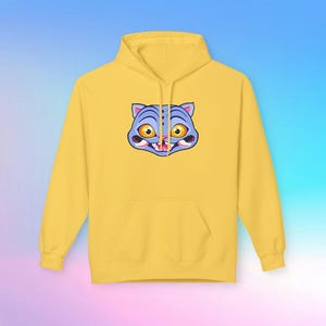 May include: A yellow hoodie with a front pocket and a drawstring hood. The hoodie features a cartoon cat face graphic in blue, orange, and white on the front. The cat has large, expressive eyes and a slightly open mouth.