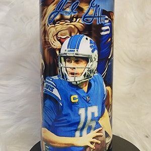 May include: A blue and white tumbler with a photo of a football player wearing a blue jersey and helmet. The tumbler has the word "Lions" printed on it and the player's signature.