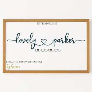 Puede incluir: Una impresión enmarcada con el texto "Introducing lovely parker" en una fuente cursiva azul oscuro. El texto va seguido de un símbolo de corazón y una fila de corazones más pequeños. El texto "ROMANTIC HANDWRITTEN FONT by Samas" está impreso debajo del texto principal.