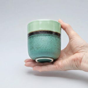 Puede incluir: Una taza de cerámica blanca con un asa negra y el texto "But First, Coffee" en negrita negra. La taza se encuentra sobre un fondo neutro, resaltando su diseño simple.