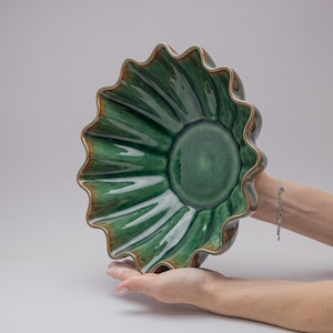Op de afbeelding: Een keramische kom met een geschulpte, golvende rand en een diep, glanzend groen glazuur. De binnenzijde is voorzien van stralende, gegroefde ribbels die verlopen van donker bosgroen in het midden naar lichtere smaragdgroene tinten aan de rand.