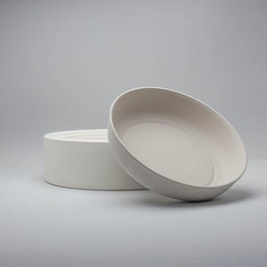Pode incluir: Duas tigelas de cer&acirc;mica branco-sujo. Uma &eacute; cil&iacute;ndrica, a outra &eacute; uma tigela rasa inclinada. As tigelas t&ecirc;m um acabamento liso e fosco. O design &eacute; minimalista e moderno, adequado para servir alimentos ou como pe&ccedil;as decorativas.