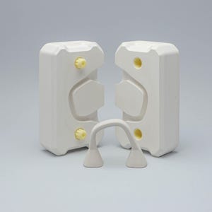 May include: Two white plastic molds with yellow accents, designed to create a pair of glasses. The molds are open and a pair of white plastic glasses are sitting in front of them.
