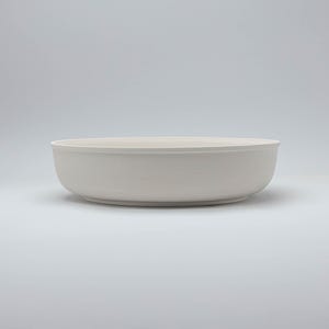Pode incluir: Uma tigela grande de cer&acirc;mica branca suja com um design largo e raso. A tigela tem um acabamento liso e fosco e uma est&eacute;tica simples e minimalista. A tigela &eacute; adequada para servir saladas, massas ou outros pratos.