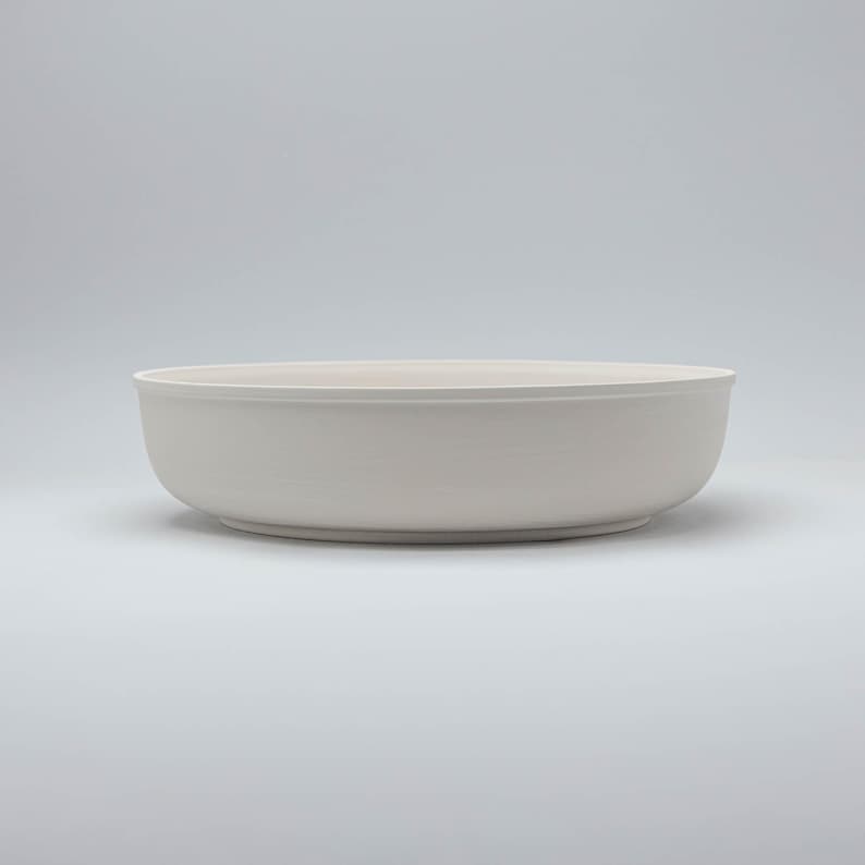Pode incluir: Uma tigela grande de cer&acirc;mica branca suja com um design largo e raso. A tigela tem um acabamento liso e fosco e uma est&eacute;tica simples e minimalista. A tigela &eacute; adequada para servir saladas, massas ou outros pratos.