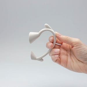 以下が含まれることがあります： 顔の筋肉をストレッチして強化するために設計された、2つの丸い端を持つ白いシリコンツールです。