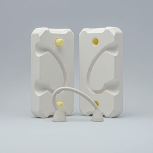 Può includere: Due stampi in plastica bianca con una forma curva e accenti gialli. Un anello in plastica bianca collega i due stampi.