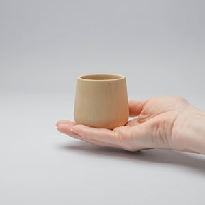 May include: A light brown wooden cup with a rounded bottom and a slightly flared top.