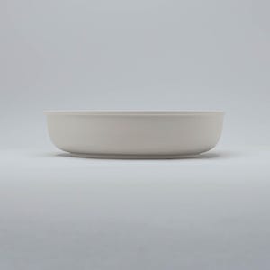 Pode incluir: Uma tigela de cer&acirc;mica cinza claro, com um design raso. A tigela tem uma base arredondada e laterais suavemente inclinadas. A borda &eacute; ligeiramente mais larga que o corpo. A tigela est&aacute; vazia e sobre uma superf&iacute;cie branca.