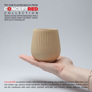 Puede incluir: Un molde de yeso beige para fundición de arcilla en barbotina. El molde tiene forma de taza con nervaduras verticales. El molde está siendo sostenido en la mano de una persona.
