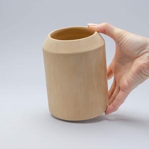 Op de afbeelding: Een lichtbruine keramische vaas met een cilindrische vorm. De vaas is glad en heeft een licht getextureerd oppervlak.