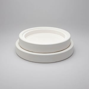 May include: Two stacked circular white ceramic plates with smooth, matte surfaces. The top plate is smaller in diameter than the bottom plate, and both feature a raised, flat-edged rim design that creates a clean, uniform, and solid white appearance.
