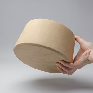 Puede incluir: Un cuenco de madera marrón claro con fondo redondeado y borde ligeramente acampanado. El cuenco está siendo sostenido por una mano.