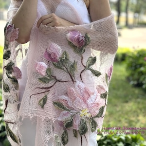 May include: A delicate pink knitted shawl with embroidered floral designs. The shawl features pink and white flowers with green leaves. The text "Наталія Вишнепольська "ЛЕГЕНДА БОТАНІЧНОГО САДУ" is visible at the bottom of the shawl.