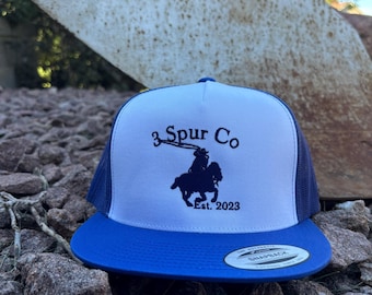 May include: A white and blue trucker hat with a black embroidered logo that says "3 Spur Co. Est. 2023" and a silhouette of a cowboy riding a horse.
