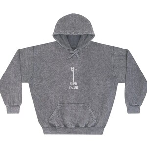 May include: A gray hooded sweatshirt with a front pocket and drawstring. The sweatshirt features a white graphic of a utility pole and the text "STORM CHASER" printed below it. The fabric has a textured, stone-washed appearance.