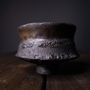 May include: A dark gray ceramic bowl with a wide, flared rim and a textured surface. The bowl has a subtle sheen and a slightly uneven base.