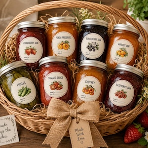 May include: A woven wicker basket containing eight glass jars of preserves, jam, sauce, and pickles, each with a round label featuring botanical illustrations and text. A burlap bow with a tag reading Made With Love is tied to the front.
