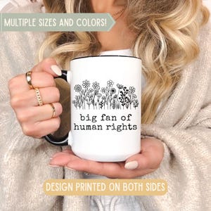 May include: White ceramic mug with a black handle and rim, featuring a floral design and the text "big fan of human rights." The mug has the text "MULTIPLE SIZES AND COLORS!" and "DESIGN PRINTED ON BOTH SIDES".
