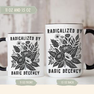 Może przedstawiać: Dwa białe ceramiczne kubki z czarnymi uchwytami i obwódkami. Kubki mają napis "RADICALIZED BY BASIC DECENCY" z czarnym kwiatowym wzorem. Jeden kubek ma 312 ml, drugi 425 ml.