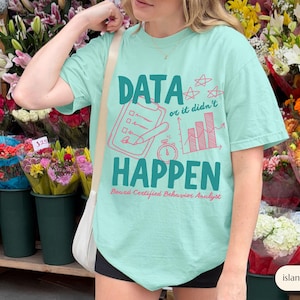 Pode incluir: Uma t-shirt verde menta claro com o texto em azul-petróleo escuro "DATA" e "HAPPEN" e o texto em vermelho "or it didn't" e "Board Certified Behavior Analyst". O gráfico inclui uma prancheta, um cronómetro, um gráfico e estrelas.