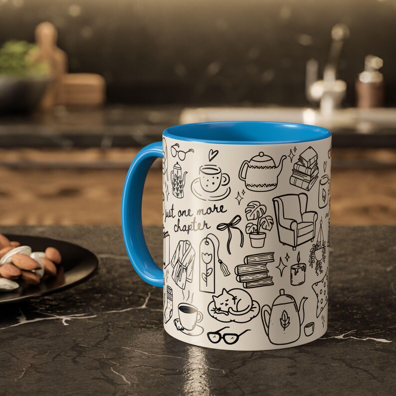 May include: White ceramic mug with a blue interior and handle. The mug features black line drawings of books, teacups, and reading-related items. The text "just one more chapter" is printed on the mug.