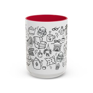 May include: White ceramic mug with a red interior, decorated with black line drawings of cosy items such as books, teapots, a fireplace, and an armchair. The mug is designed for hot drinks.