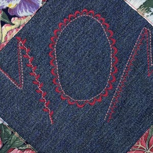 May include: A quilted square with the word "MOM" embroidered in red thread on a denim patch. The denim patch is surrounded by floral fabric in shades of pink, purple, and green.