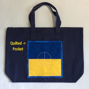 May include: Navy blue tote bag with a zippered top and two navy blue handles. The front features a quilted pocket with a blue and yellow design and a white peace symbol.