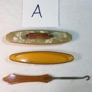 May include: A set of three vintage shoe horn tools. The tools are made of amber-colored plastic and have a smooth, glossy finish. The set includes a shoe horn with a handle, a small shoe horn, and a larger shoe horn with a lid.