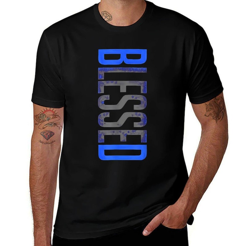 May include: Black t-shirt with the word "BLESSED" printed vertically in a blue and gray color scheme. The text is centered on the front of the shirt. The shirt has short sleeves and a crew neck.