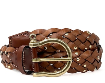 May include: A brown leather belt with a woven design. The belt features a gold-colored buckle and small gold-colored rivets. The leather is a rich, warm brown color.