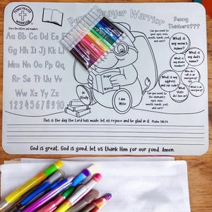 May include: A white educational placemat with a cartoon elephant reading a book, titled "Prayer Warrior." Includes alphabet, numbers, and fill-in-the-blank questions. A set of colorful markers is included. The text reads "God is great, God is good, let us thank Him for our food. Amen."