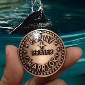 May include: A copper-colored coin with the words "Penny Prayer Warrior" inscribed on it. The coin has a decorative border of small dots and stars.
