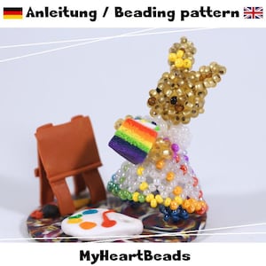Könnte beinhalten: Eine Perlenfigur eines Hasen, der ein regenbogenfarbenes Kuchenstück hält, neben einer braunen Staffelei und einer weißen Farbpalette. Der Text "Anleitung / Beading pattern" und "MyHeartBeads" ist im Bild zu sehen.
