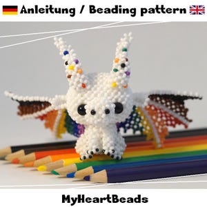 Op de afbeelding: Een klein drakenfiguurtje gemaakt van witte kralen met grote zwarte ogen en twee hoorns met gekleurde stippen. De draak heeft wijd uitgestrekte vleugels met een levendig regenboogverloop. De tekst "Anleitung / Beading pattern" en "MyHeartBeads" staan in de afbeelding.