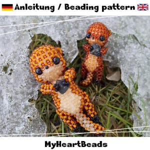May include: Two beaded otter figurines in shades of orange, brown, and cream, with black accents. One otter lies on its back, while the other stands holding a dark stone. The image includes the text "Anleitung / Beading pattern" and "MyHeartBeads".