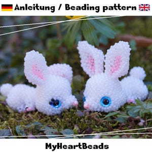 Peut inclure: Deux figurines de lapin blancs perlés, avec l'intérieur des oreilles roses et des yeux bleus, posées sur de la mousse. Le texte "Anleitung / Beading pattern" indique un modèle de perlage. Le logo MyHeartBeads est en bas.