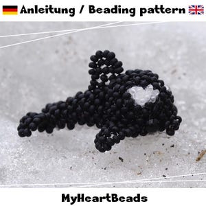 May include: A beaded orca whale figurine, primarily black with white accents, including the belly and eye markings. The text "Anleitung / Beading pattern" is at the top, and "MyHeartBeads" is at the bottom.