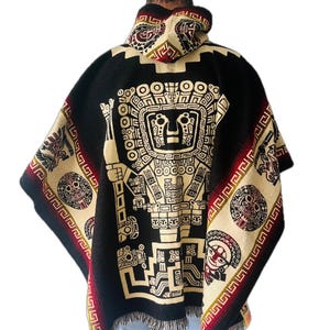 Op de afbeelding: Zwarte poncho met capuchon, met een groot crèmekleurig centraal ontwerp van een gestileerde figuur. De poncho heeft crèmekleurige randen met geometrische patronen en rode accenten. Het kledingstuk is gemaakt van een dik, geweven materiaal.