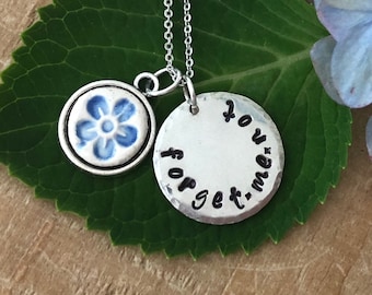 May include: Silver necklace with a forget-me-not charm and a round pendant that says "forget-me-not".