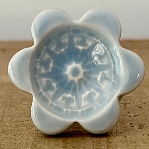 Può includere: Pomello a forma di fiore in ceramica azzurra con un motivo floreale dettagliato azzurro e bianco al centro. Il pomello è appoggiato su una superficie di legno.