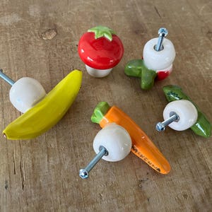 Pu&ograve; includere: Una collezione di pomelli per armadietti in ceramica stravaganti a forma di frutta e verdura. Include una banana gialla, un pomodoro rosso, asparagi verdi e una carota arancione. Ogni pomello ha una vite argentata per il montaggio.