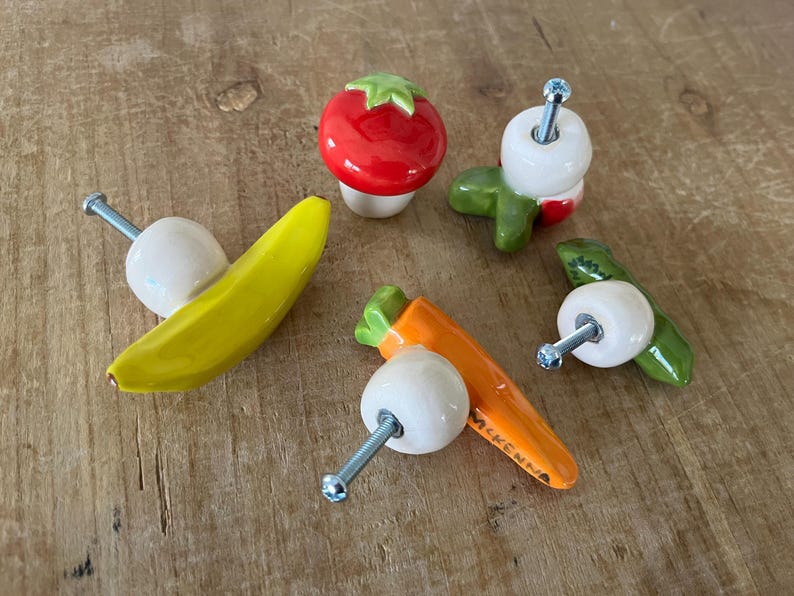 Pu&ograve; includere: Una collezione di pomelli per armadietti in ceramica stravaganti a forma di frutta e verdura. Include una banana gialla, un pomodoro rosso, asparagi verdi e una carota arancione. Ogni pomello ha una vite argentata per il montaggio.