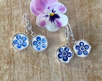 May include: A pair of silver dangle earrings with blue and white floral designs. The earrings have a silver hook closure.
