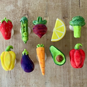 Pu&ograve; includere: Una collezione di pomelli per mobili in ceramica a forma di verdura colorata. Il set include una fragola rossa, un baccello di piselli verde, una barbabietola rossa, una fetta di limone giallo, broccoli verdi, peperone giallo, melanzana viola, carota arancione, avocado verde e peperone rosso.